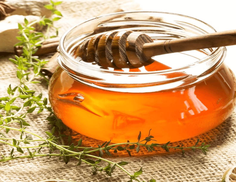 honey in a jar with herbs around it.
